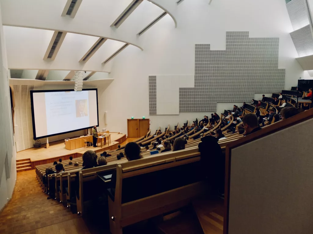 Many students in a lecture hall, facing a large screen