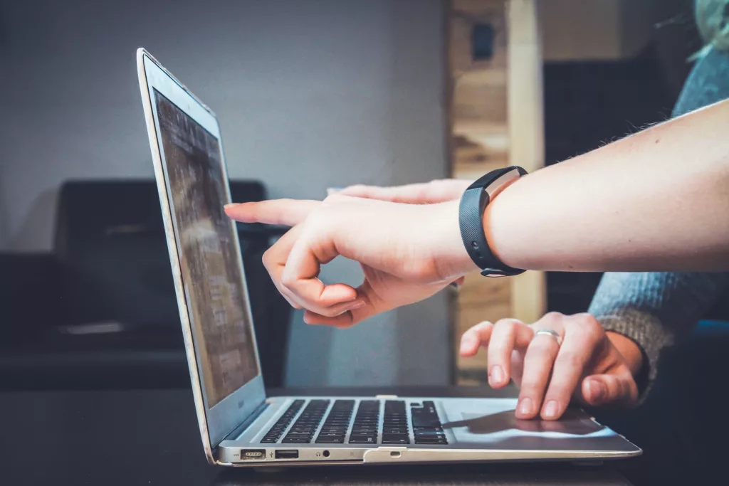 A hand points at a laptop screen