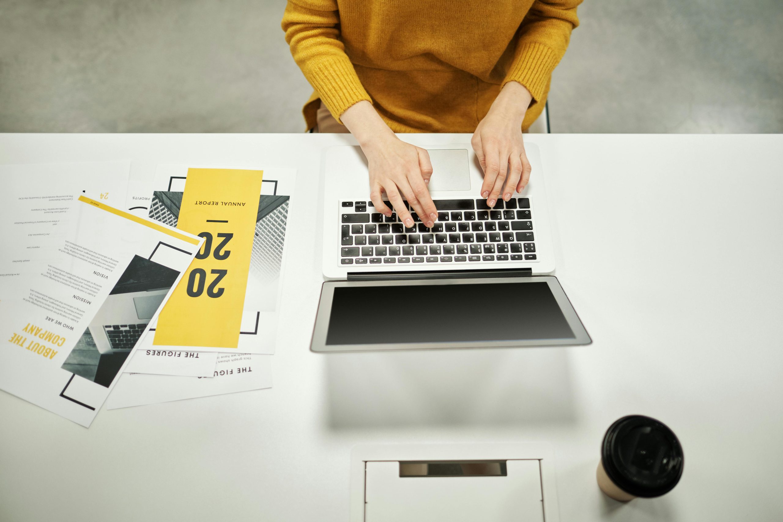 Woman in a yellow sweater typing an annual report on a laptop