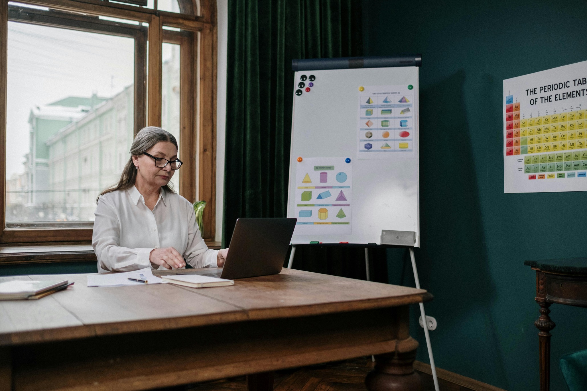 Female professor using a laptop while seated at a table in a classroom