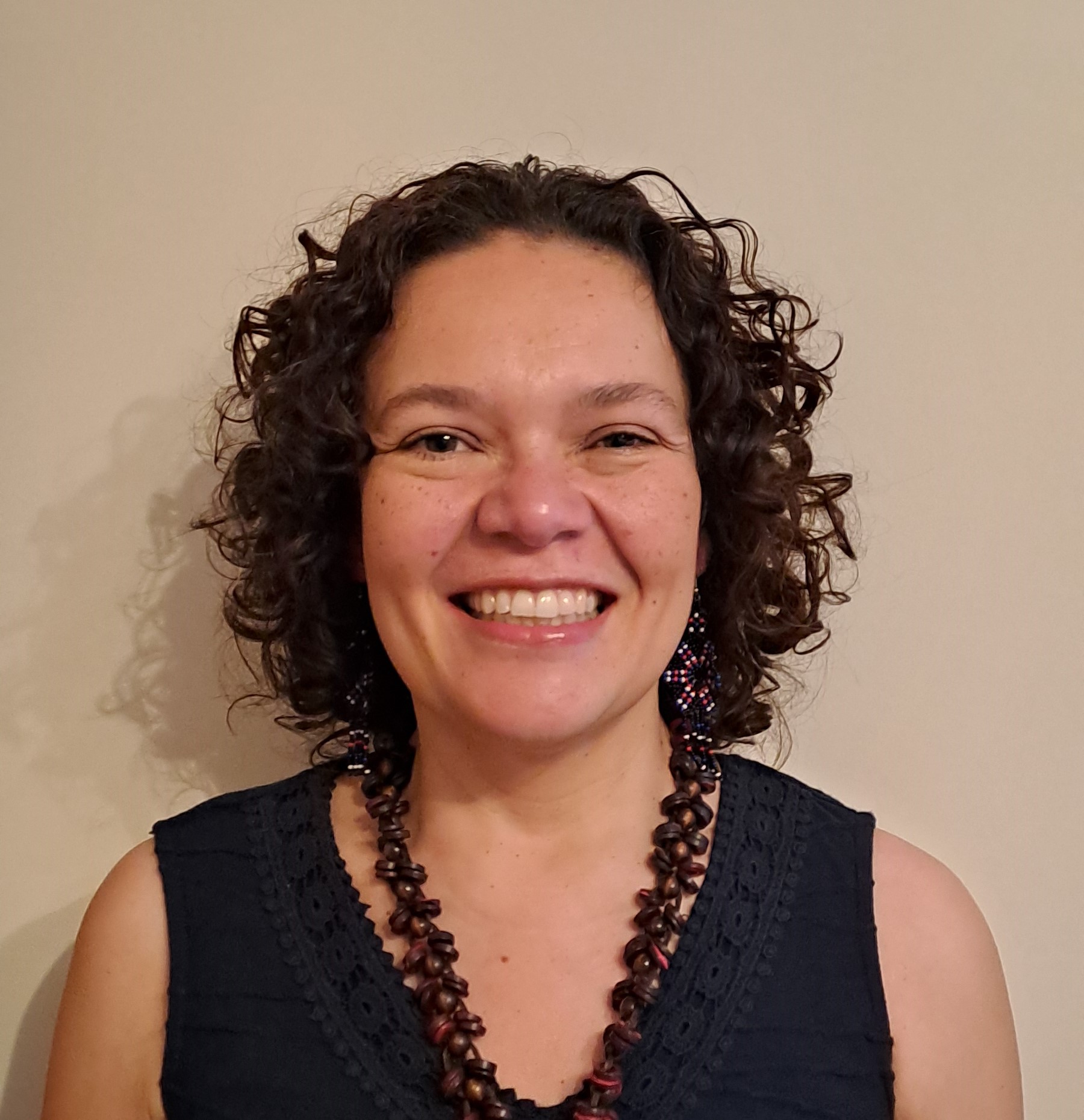 woman smiling with short curly hair, blue shirt and necklace