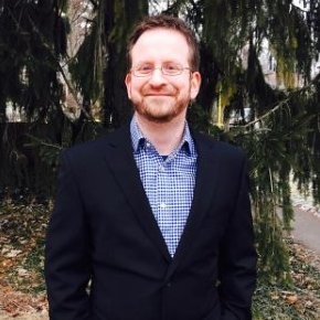 Man wearing glasses, blue sweater and light blue button up shirt