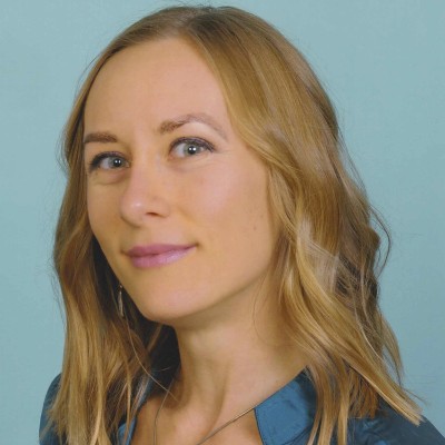 Blond woman wearing a dark blue shirt in front of a light blue background