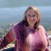 A photo of a woman with a purple sweater in front of a coastline